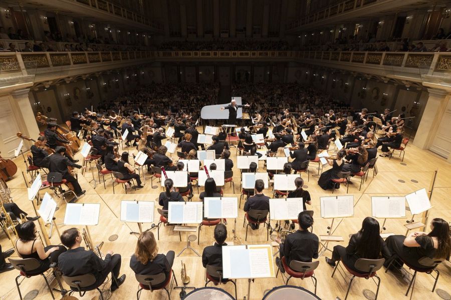 Blick auf Orchester, Dirigent und Publikum von hinter der Bhne